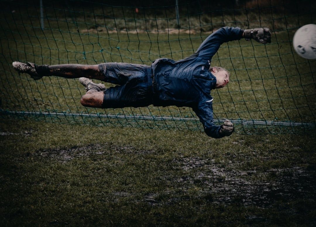 Målvakt kastar sig vågrätt mot en fotboll på lerig plan